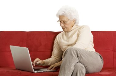 Elderly woman on the couch with laptop clipart