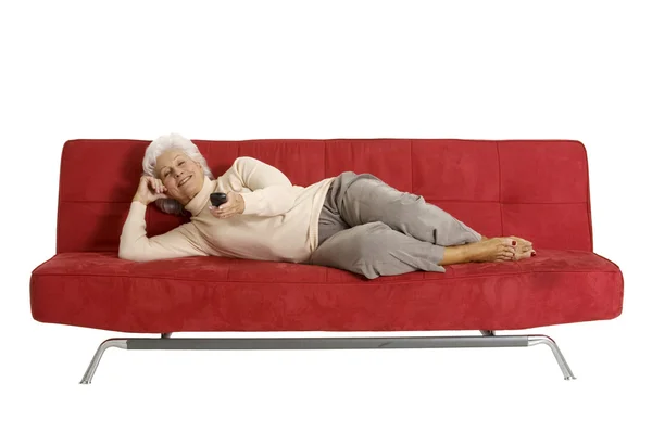 Idős nő a kanapé, a televízió távirányítóval — Stock Fotó