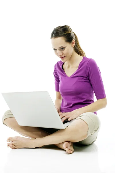 Молодая женщина сидит на полу с ноутбуком на белом фоне студии — стоковое фото