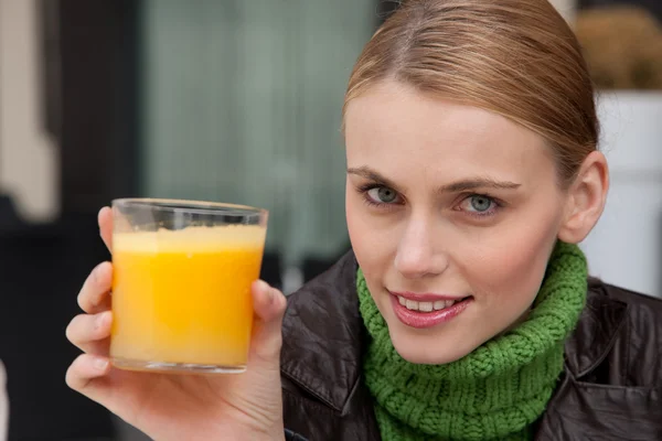 Młoda kobieta trzymając szklankę soku pomarańczowego i patrząc na kamery — Zdjęcie stockowe