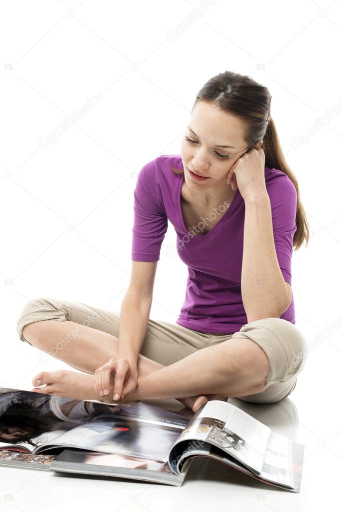 Young woman sitting on the floor reading a magazine on white background stu