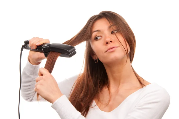 若いブルネットの女性を白い背景で隔離の新しいスタイリッシュなヘアスタイルを作る毛矯正黒い平らな鉄を使用して — ストック写真