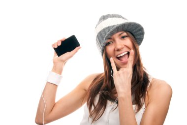 Pretty rock girl showing cellular mobile phone and in rock n roll sign finger smiling in headphones and hat isolated on a white background. clipart