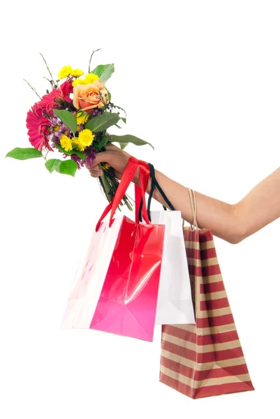 Mano sosteniendo coloridas bolsas de compras y flores — Foto de Stock