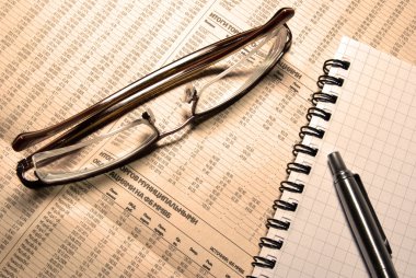 Glasses, pen and notebook laying on newspaper with financial num clipart