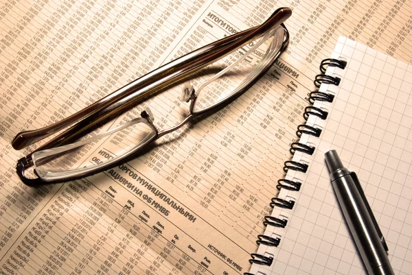 Brille, Stift und Notizbuch auf Zeitung mit finanzieller Nummer — Stockfoto