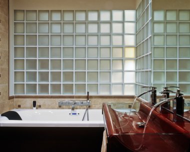 Modern bathroom with red washbasin and bathtub under a wall of glassblock clipart