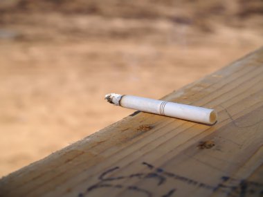 A smoldering cigarette left carelessly on a wooden window sill. clipart