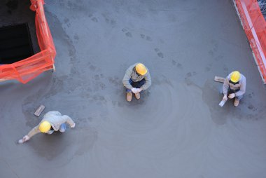 Three workers with one smoothing out freshly poured concrete. clipart