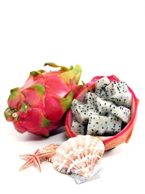 Diced dragon fruit pieces in the shell next to a whole fruit with sea shells clipart