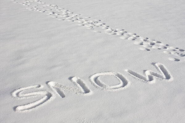 SNOW Written In A Snowy Field Beside Footprints