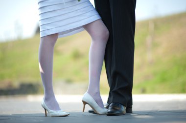 Feet of the groom and the bride adjoin knees on a dim back background clipart