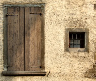 Small window and big closed window with brown shutters. Rough, yellow or beige wall of an old house in a small Italian town or village. clipart