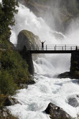 Male tourist above an extremely powerful waterfall in Briksdalen valley, Jostedalsbreen National Park in Norway. clipart
