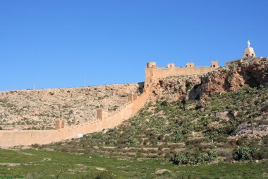 Alcazaba - fortified Moorish castle on a hill in Almeria, Andalusia, Spain. Christ statue. clipart