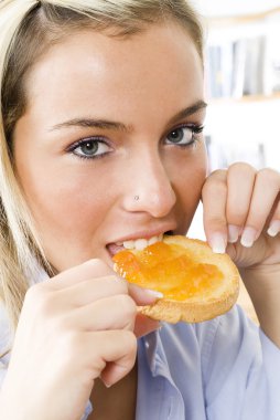 a sensul blond girl eating a toast with jam one morning during her breakfast clipart