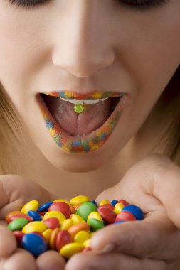 close up of colored open mouth of girl with color smarties in hand clipart