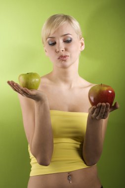 blond girl with red and green apple in act to take a decision of what kind of apple to eat red or green clipart