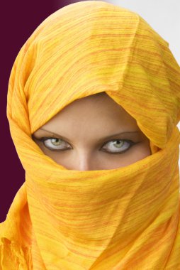 Attactive and strong eyes behind an orange scarf used like a burka clipart