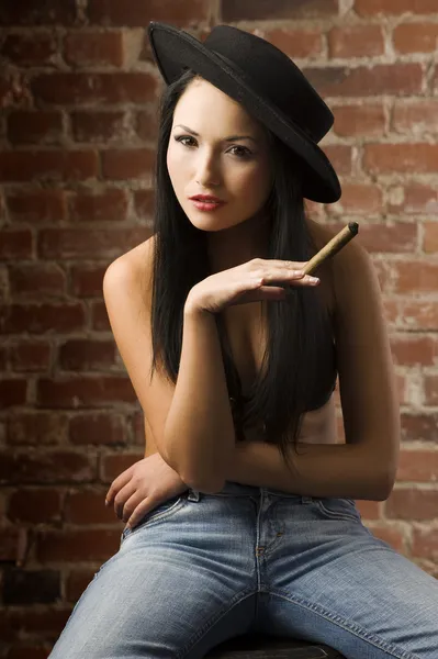 很好的亚洲女孩戴着黑色帽子坐 抽着雪茄 — 图库照片