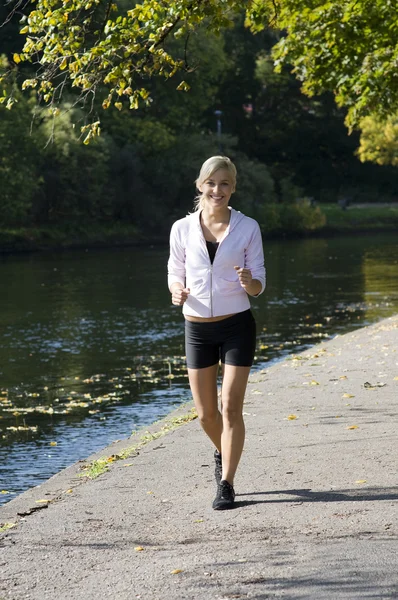 川の近くの公園で走っているかなり若いブロンドの女の子 — ストック写真