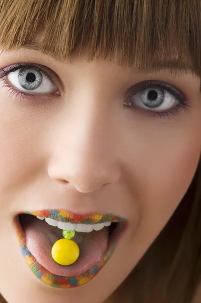 多色の唇と舌の上の黄色のキャンディーを持つ若い女の子のクローズ アップ — ストック写真