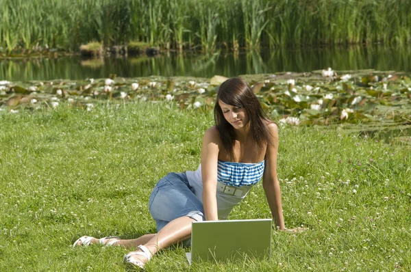 草に単独で立っていると コンピューターに取り組んでいるカジュアルな服装でかわいいブルネット — ストック写真
