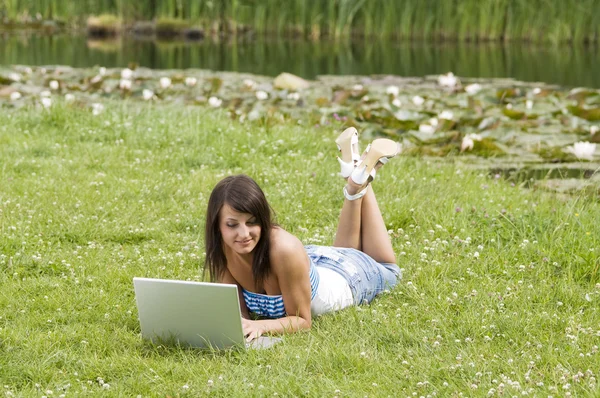 可爱布鲁内特穿便服在草地上 独自站在和在计算机上工作 — 图库照片