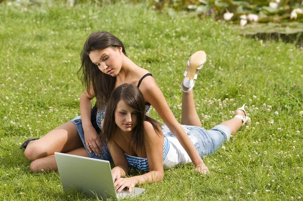 两个好学生女孩躺在草和学习用的笔记本电脑 — 图库照片