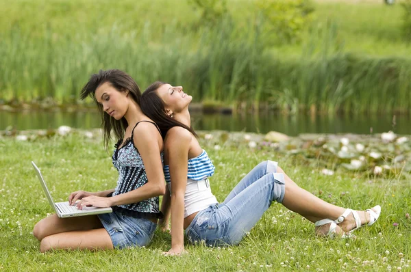 Две Симпатичные Девушки Сидящие Траве Спиной Спине Одна Другой Работая — стоковое фото