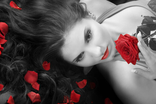 Portrait of a young pretty woman with red rose on black background