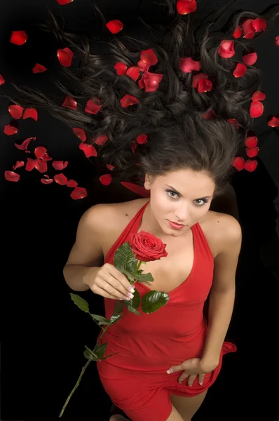 薔薇と髪の花弁を持つエレガントな赤いドレスで美しい若い女性 — ストック写真