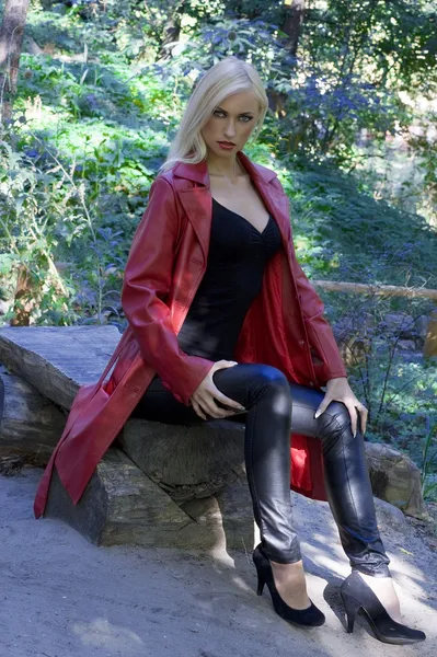 長い赤い皮のコートを着て撮影ファッションで公園の外ブロンドのセクシーな女性 — ストック写真