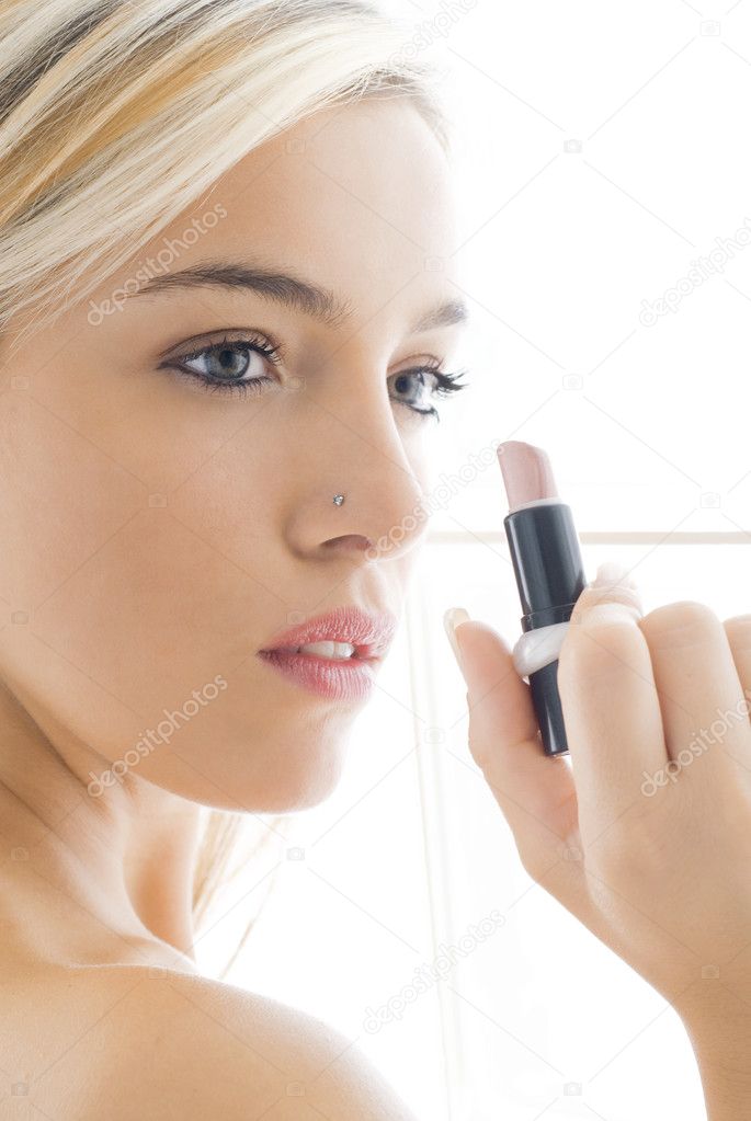 high key close up of a pretty girl painting her lips with pink lipstik