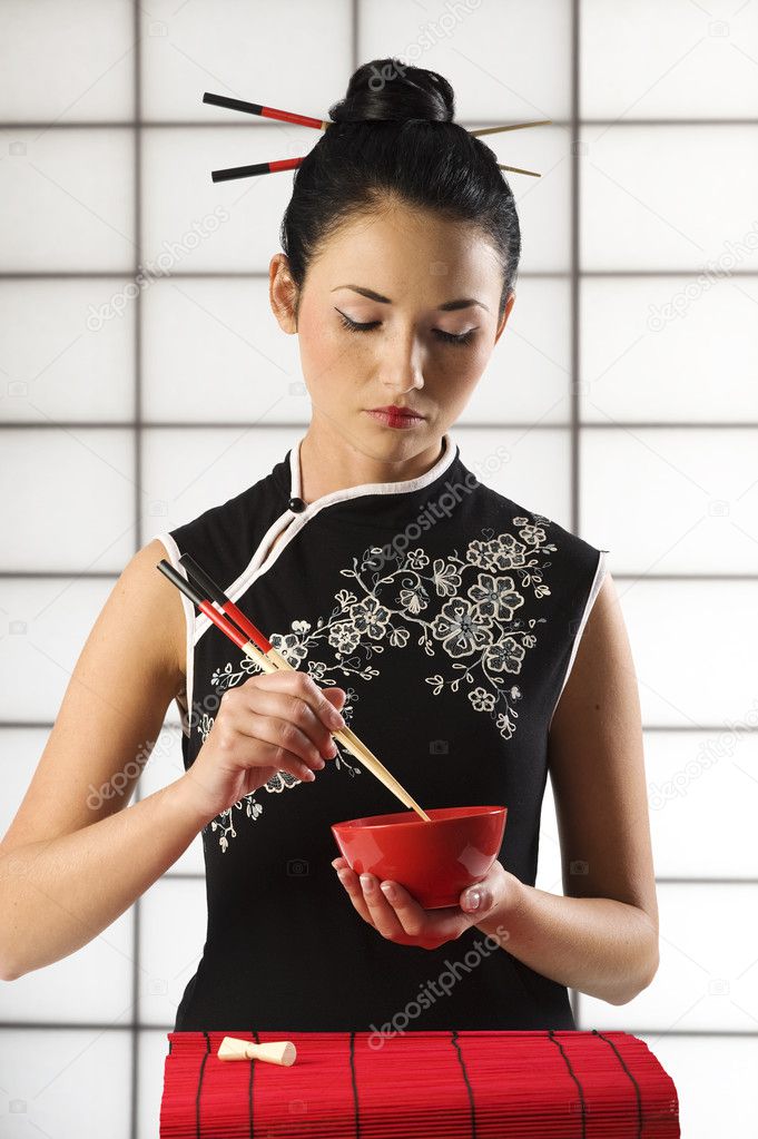 beautiful asian girl in calssic oriental dress in act to eat with chopstick