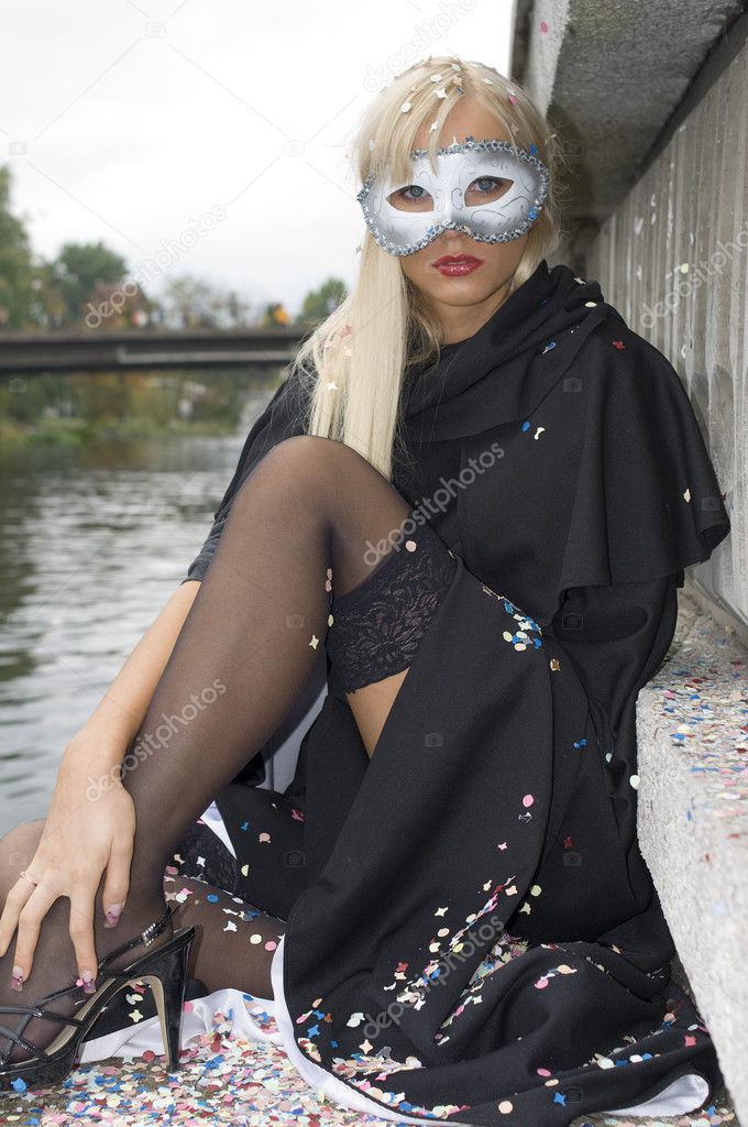sexy blond girl near river with carnival mask and black cloak showing legs