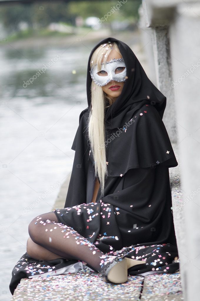 blond girl near river under black hood with colored confetti all around