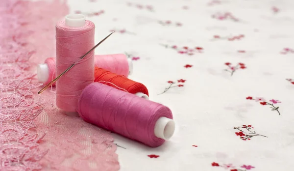 Carretel rosa de fio em um tecido floral — Fotografia de Stock