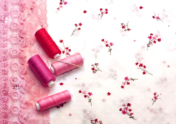 Pink spools of thread on a floral fabric — Stock Photo, Image