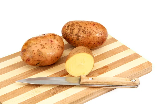 Tuberi di patate crude sdraiati su un tagliere — Foto Stock