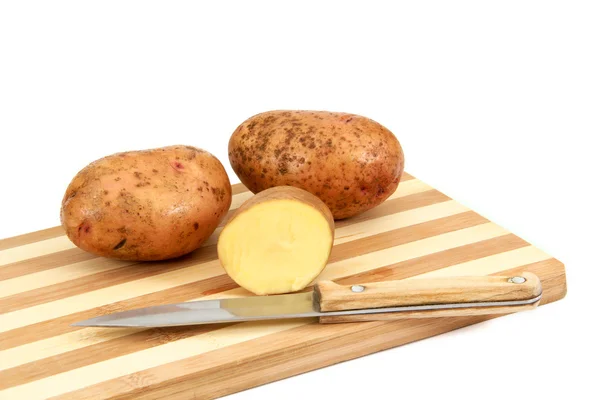 Tuberi di patate crude sdraiati su un tagliere — Foto Stock