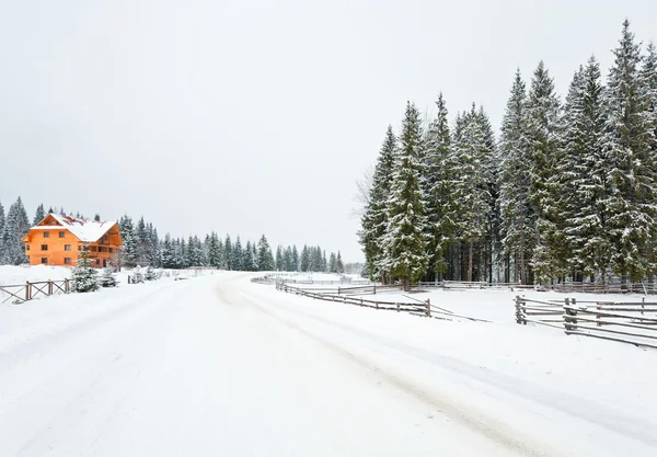 Winter dull mountain landscape with fence , wooden house and country road