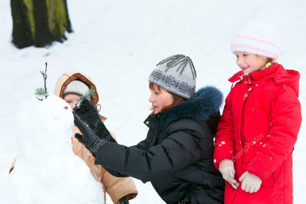 Family (mother with small children) sculpting snowmen in winter city park