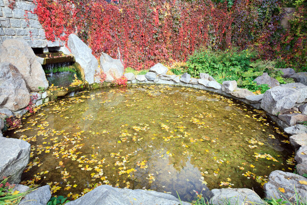 Pond water surface with yellow leafs and small waterfall in autumn park