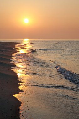 Misty daybreak sea sandy shore with sunlight path and fishing boat distant silhouette clipart