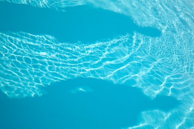 Patterns of sunlight rippling o n a swimming pool water surface with two human shadows clipart