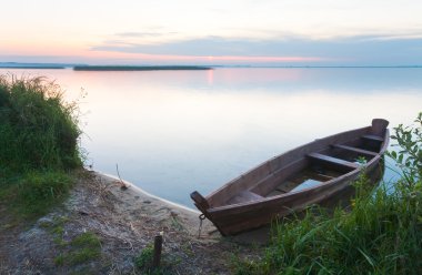 Sunset with old flooding boat on summer lake shore clipart