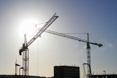 Sun behind cranes on construction site (with lens flare effect on right) clipart