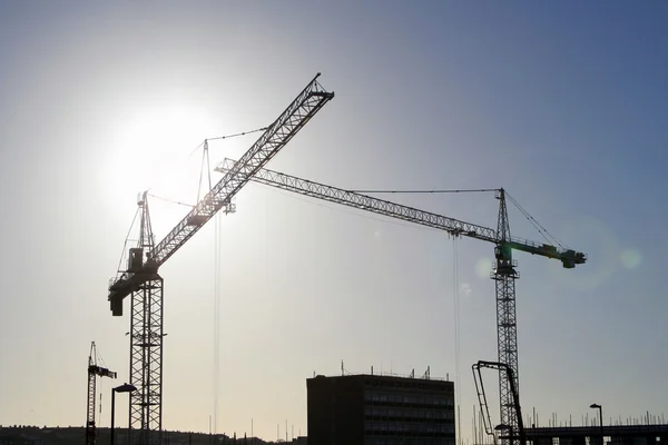 Sun behind cranes on construction site (with lens flare effect on right) — Stock Photo, Image