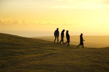 Group of friends caught against dramatic backlighting at early evening walk in countryside clipart